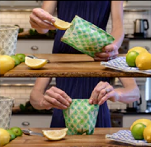 Person using a green reusable wrap in a kitchen setting with lemons and limes on wooden cutting boards.